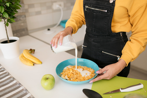 Close up of a young Caucasian woman in her kitchen at home, preparing herself some breakfast cereal with fruit