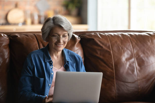 istock Smiling elderly woman in glasses using laptop at home 1277387039