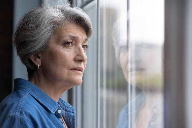 regard âgé triste de femme dans la fenêtre manquant ou pensant - women depression window sadness photos et images de collection