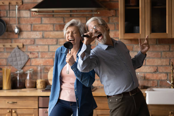 la pareja de ancianos alegres se divierten cantando en la cocina de casa - action senior adult lifestyles couple fotografías e imágenes de stock