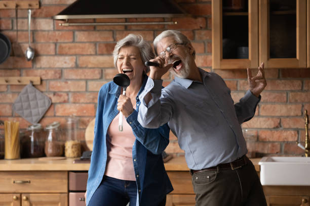 Overjoyed senior couple have fun singing at home kitchen