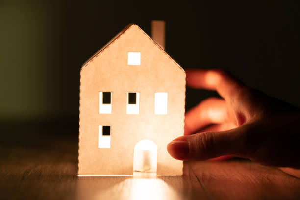 istock Fragile bright white paper home illuminated from inside over dark background, supported by hand. House security, comfort and peace. 1277387217