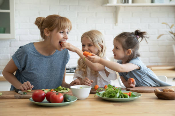 hijas cariñosas alimentando a mamá con verduras - healthy eating snack child domestic kitchen fotografías e imágenes de stock