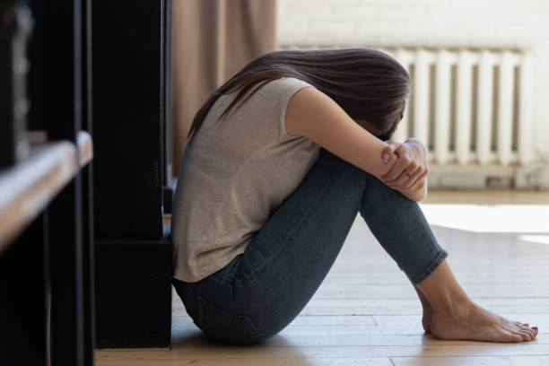 istock Distraught lady with arms around knees sitting alone on floor 1277398405