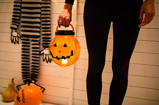 A cropped shot of a woman holding a see-through plastic Halloween pumpkin with a light inside