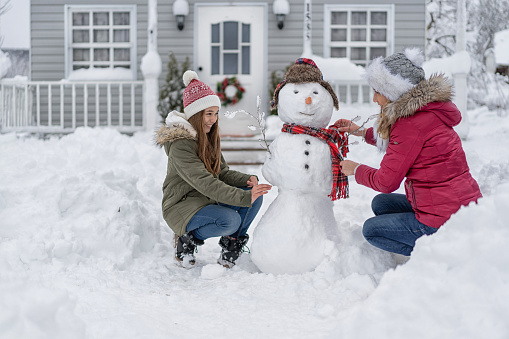 Mother and daughter making a snowman in front of the house, during COVID-19