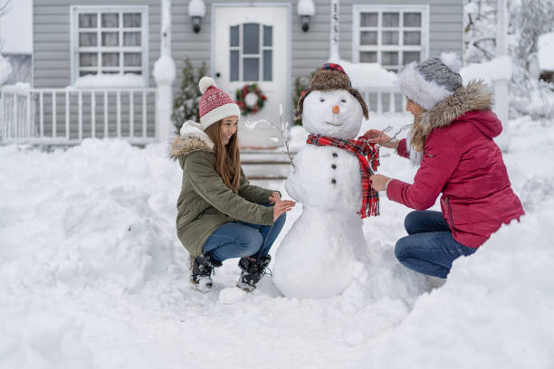 mother and daughter making a snowman in front of the house, during covid-19 - family winter walking fun imagens e fotografias de stock