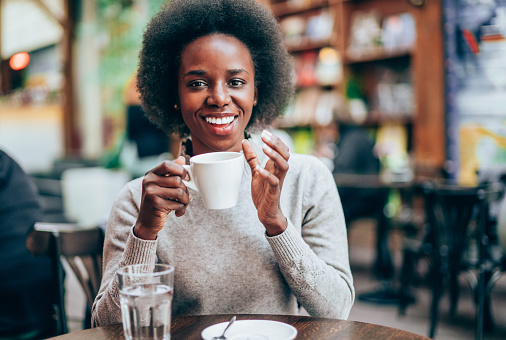 Portrait of beautiful smiling african-american woman sitting in city cafe and drinking coffee.