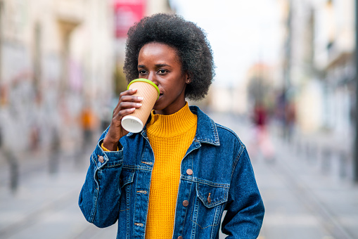 Portrait of a beautiful smiling African-American woman drinking hot coffee on the city street.