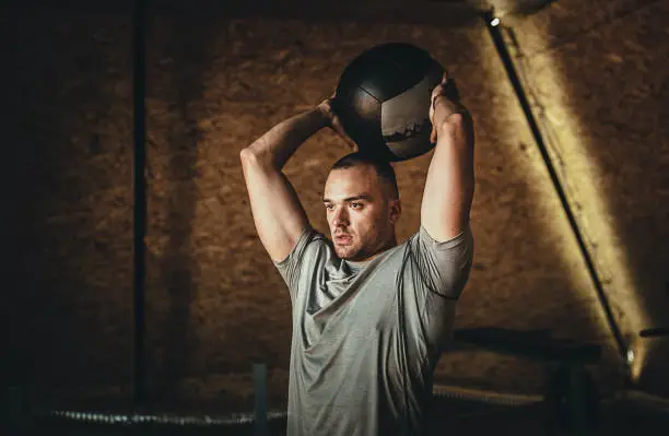 One young male athlete training with medicine ball in the gym.