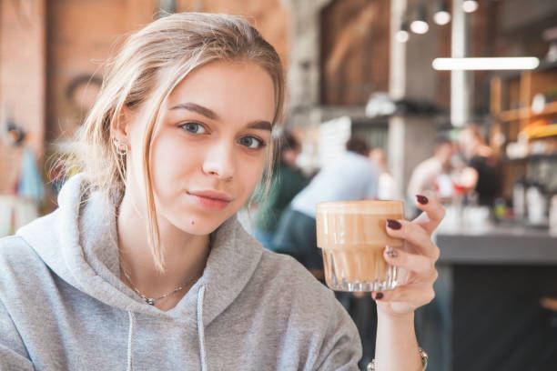 Young blond beautiful girl holds a glass of coffee Young blond beautiful girl holds a glass of coffee, close-up photo with selective soft focus 15 year old blonde girl stock pictures, royalty-free photos & images