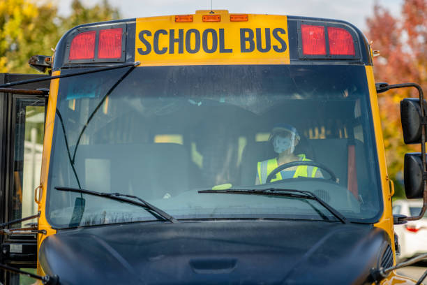 Female bus driver wearing a protective face mask and shield while driving a school bus during COVID-19 to avoid the transfer of germs.