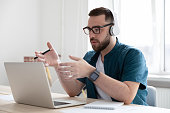 Serious businessman wearing headphones using laptop, speaking, making call