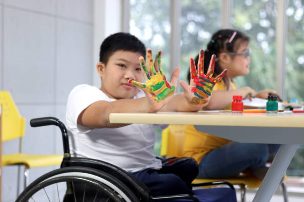 istock Disabled kids classroom, children having fun during study at school, kids learning together, schoolboy on wheelchair showing his painted hands 1277410391