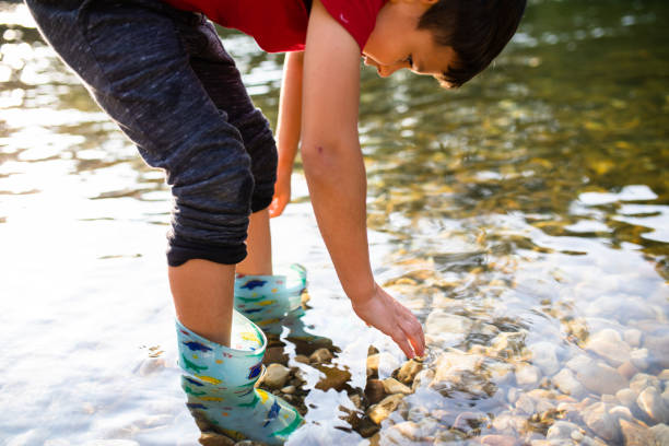 istock A young boy reaching for a rock on the riverbed in the shallows 1277411717