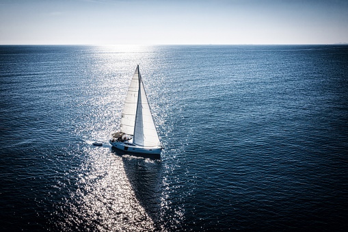 Sailboat sails gracefully across turquoise blue off the coast of South England. Favorable sailing conditions and a beautiful sunny summer day to explore the picturesque English coastline from a boat.