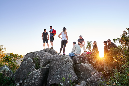 Shot of group of people sitting on mountain top and resting during sunrise hike