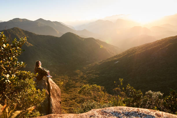Shot of a mature woman sitting on a rock at mountain top and looking at the beautiful sunrise
