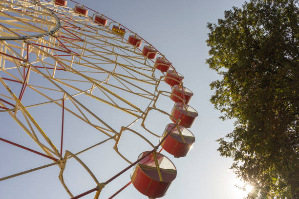 istock Closed, non - working attraction Ferris wheel with empty booths against a clear sky and a tall tree. 1277415671