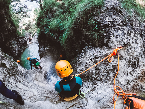 Woman canyoning in Slovenia, woman wearing neoprene and safety gear rappelling in the canyon.