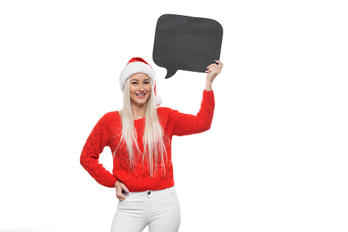 Christmas sign woman peeking over empty black chalkboard card sign wearing santa hat isolated on white background. Funny surprised and shocked look on santa girl face.