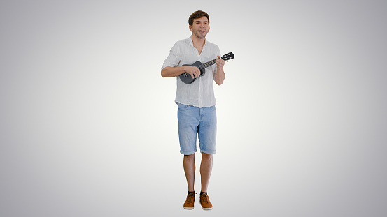 Wide shot. Front view. Smiling young man playing ukulele and singing looking into the camera on gradient background. Professional shot in 4K resolution. 047. You can use it e.g. in your medical, commercial video, business, presentation, broadcast