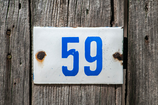 Weathered grunge square metal enameled plate of number of street address with number 59 closeup