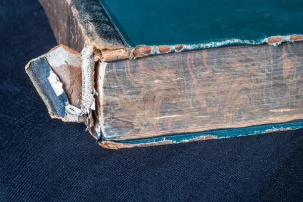 Old book with damaged spine on dark cloth. Selective focus.