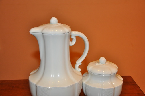 Elegant white porcelain tea or coffee pot with saucer.White teacup and teapot on table.
