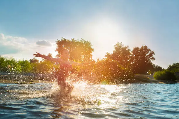 Photo of Happy child playing in the water at sunset. Summer vacation and healthy lifestyle concept.