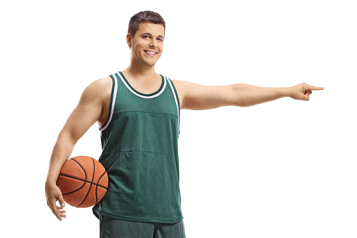 Basketball player in a jersey holding a ball and pointing to one side isolated on white background