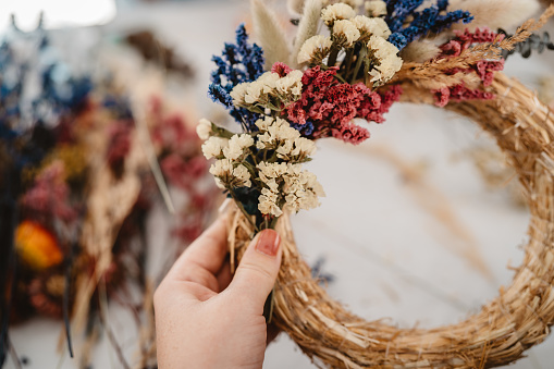 Girl making floral door wreath from colorful dry summer flowers and plants.  Fall flower decoration workshop