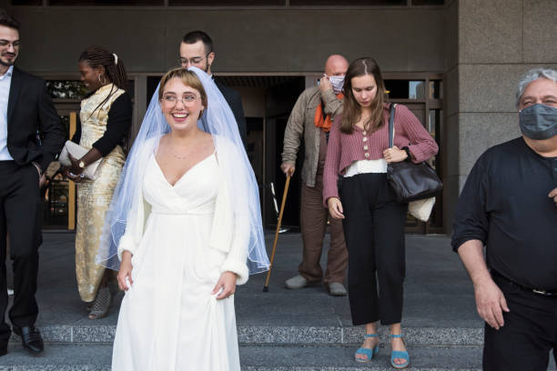 Millennial newlyweds and guests leaving courthouse after a socially distanced wedding during Covid pandemic. Part of a series. Horizontal full length outdoors shot with copy space.