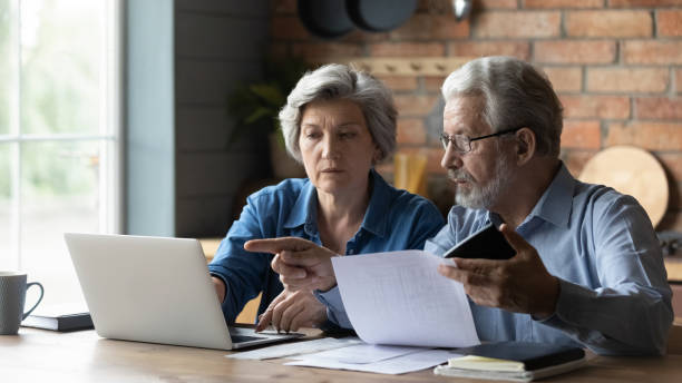 пожилые пары оплачивать счета онлайн на ноутбуке - middle human age couple women стоковые фото и изображения