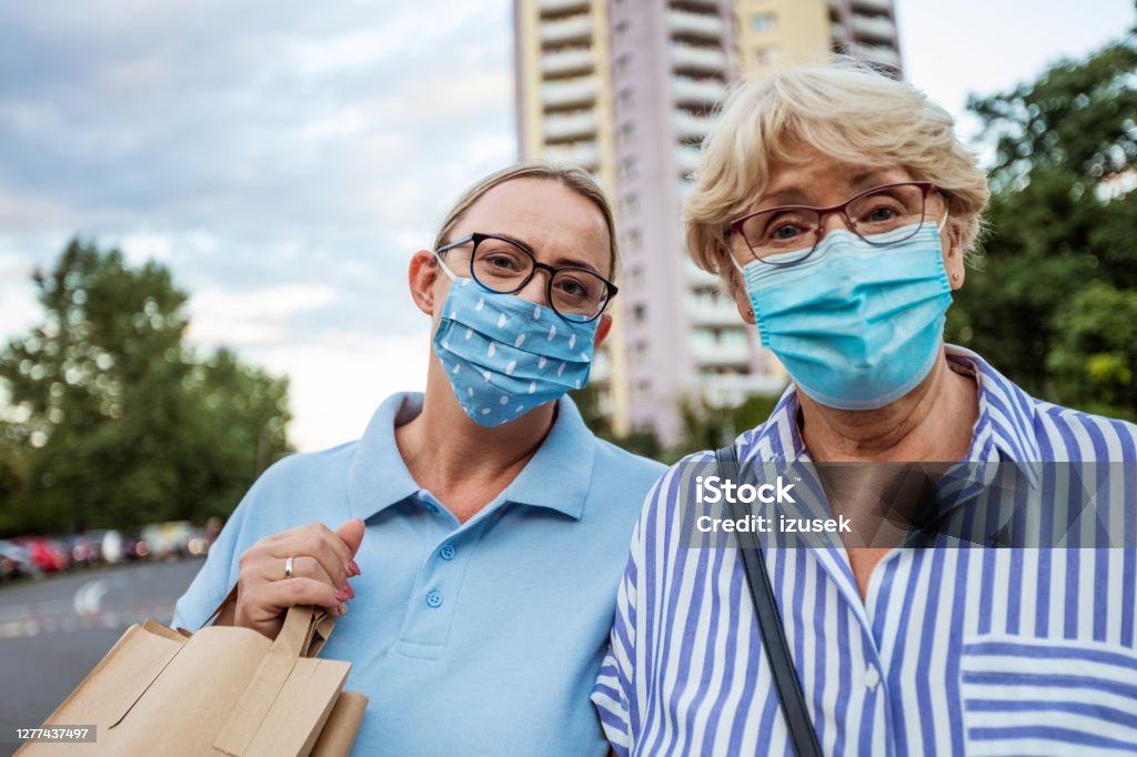 Home caregiver helping senior woman with shopping Outdoor portrait of senior woman and social worker. They are wearing protective face masks, standing in front of apartment in the city. 40-44 Years Stock Photo
