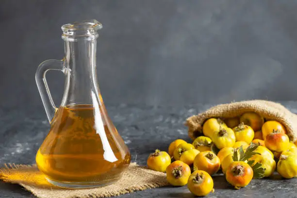 Glass bottle of hawthorn vinegar with Fresh ripe red/yellow hawthorn fruits on rustic background. Crataegus monogyna berries