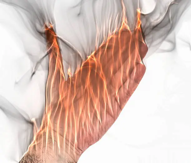 Photo of A human hand on fire burning with orange flames and some smoke in front of a bright background