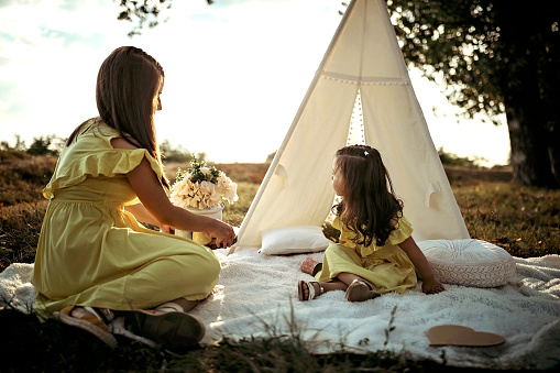 Mother and daughter resting on the blanket in meadow near tent