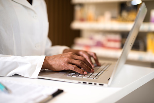 Close up of female Pharmacist / Doctor working on a laptop. Hand close up.