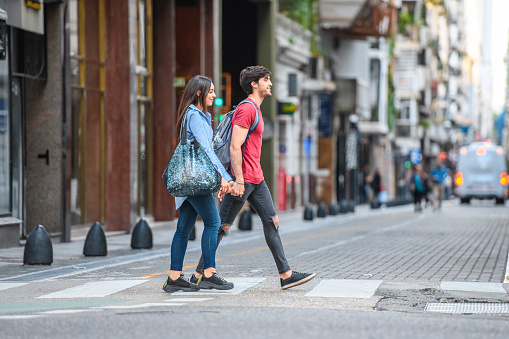 Hispanic male and female vacationers in their 20s holding hands and exploring downtown Buenos Aires on foot.