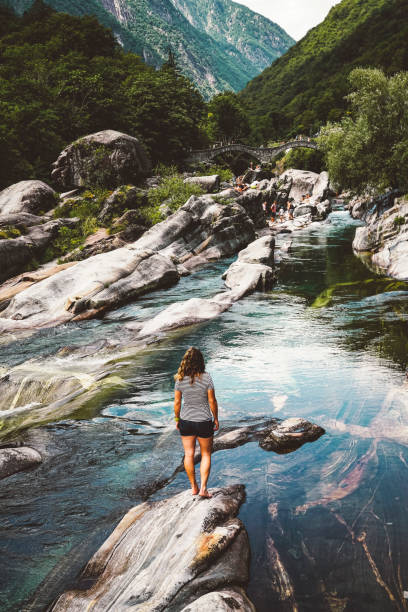 woman traveler standing on a rock overlooking the river at verzasca valley - riverbed switzerland valley stone imagens e fotografias de stock