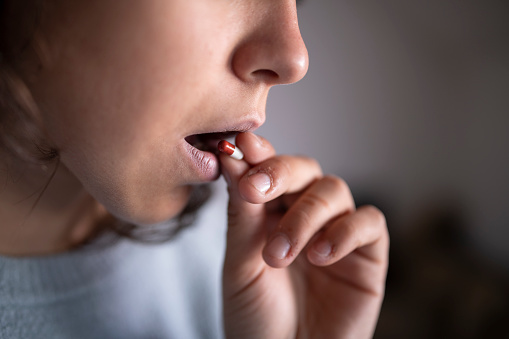 Female is taking a red and white medical pill capsule