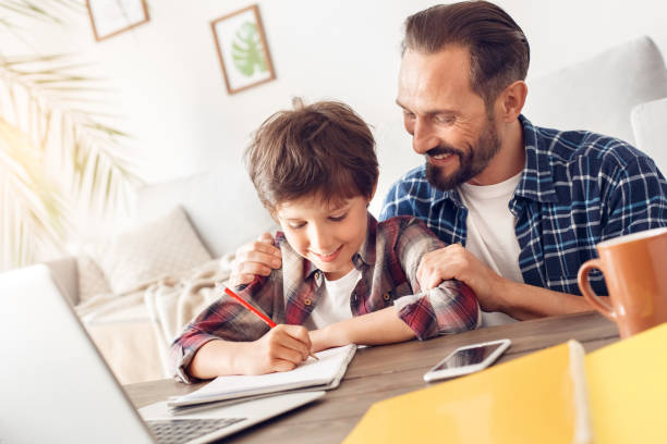 istock Father hugging son doing assignment at home sitting at table smiling cheerful 1277453535