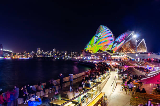 оперный театр и бар во время фестиваля vivid sydney lights с людьми, выпивая на переднем плане - opera bar стоковые фото и изображения