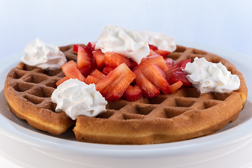Generous serving meal of a hearty strawberry waffle decorated with whipped cream on round plate.