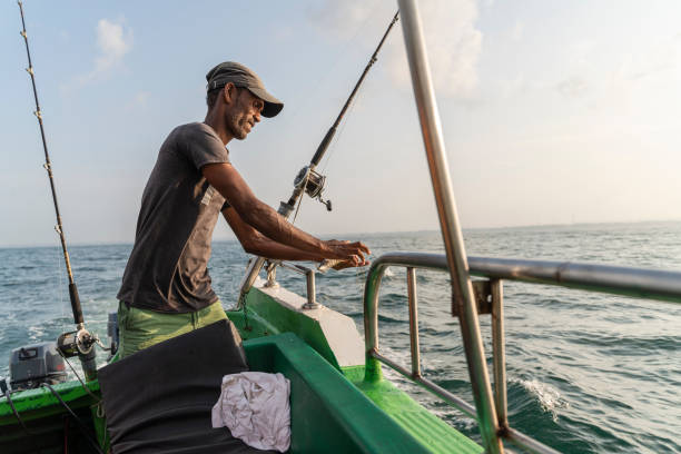 pescatore che prepara l'attrezzatura da pesca, attaccando un'esca a bordo di una barca durante la pesca d'altura nell'oceano. - pesca daltura foto e immagini stock