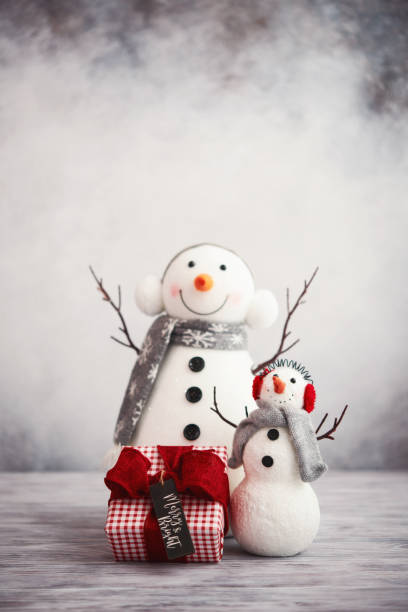 istock Cute Christmas background with snowmen pair and gift in bright setting 1277462998
