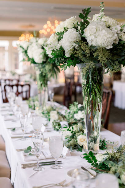 istock A beautiful wedding reception table set-up with tall clear glasses (trumpet vases) filled with greenery and white blooming flowers. A classic wedding floral arrangement. 1277469632