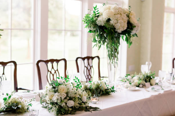 istock The head table at a wedding reception with the bride and bridesmaids bouquets on the table. The table is decorated with tall standing glass vase with a huge white and green floral arrangement. 1277469645