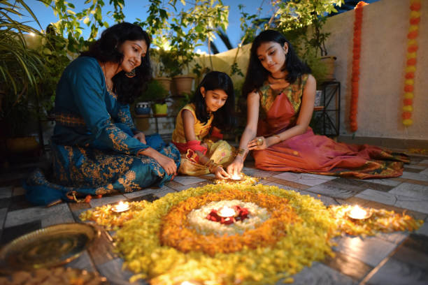 istock Mother and daughters lighting lamps around rangoli made using petals 1277472466